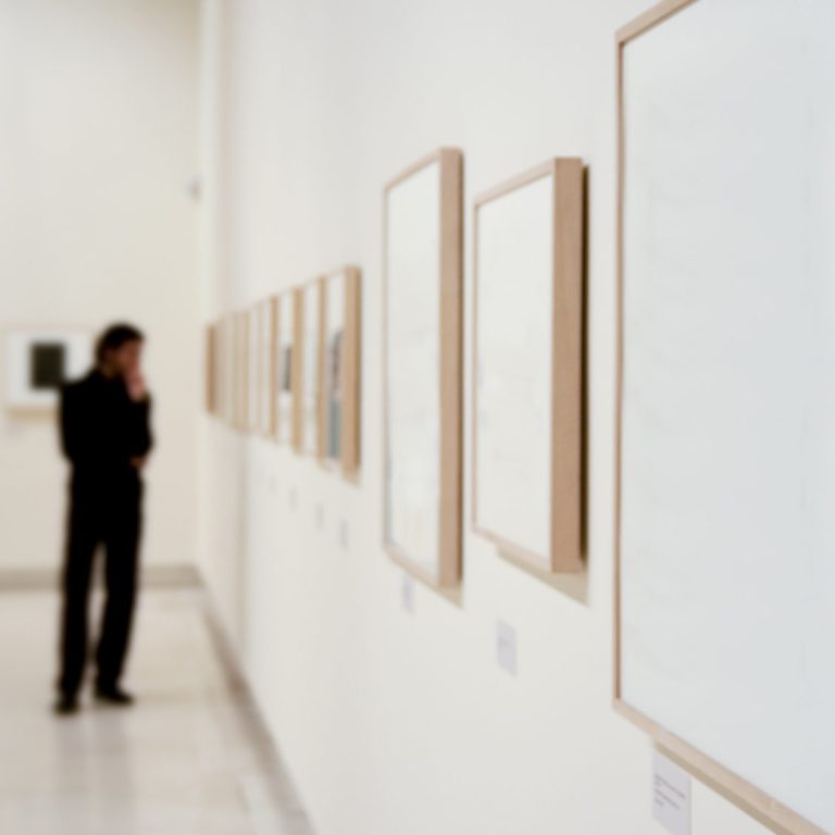 Mann steht nachdenklich vor leeren Bilderrahmen in einer Galerie.